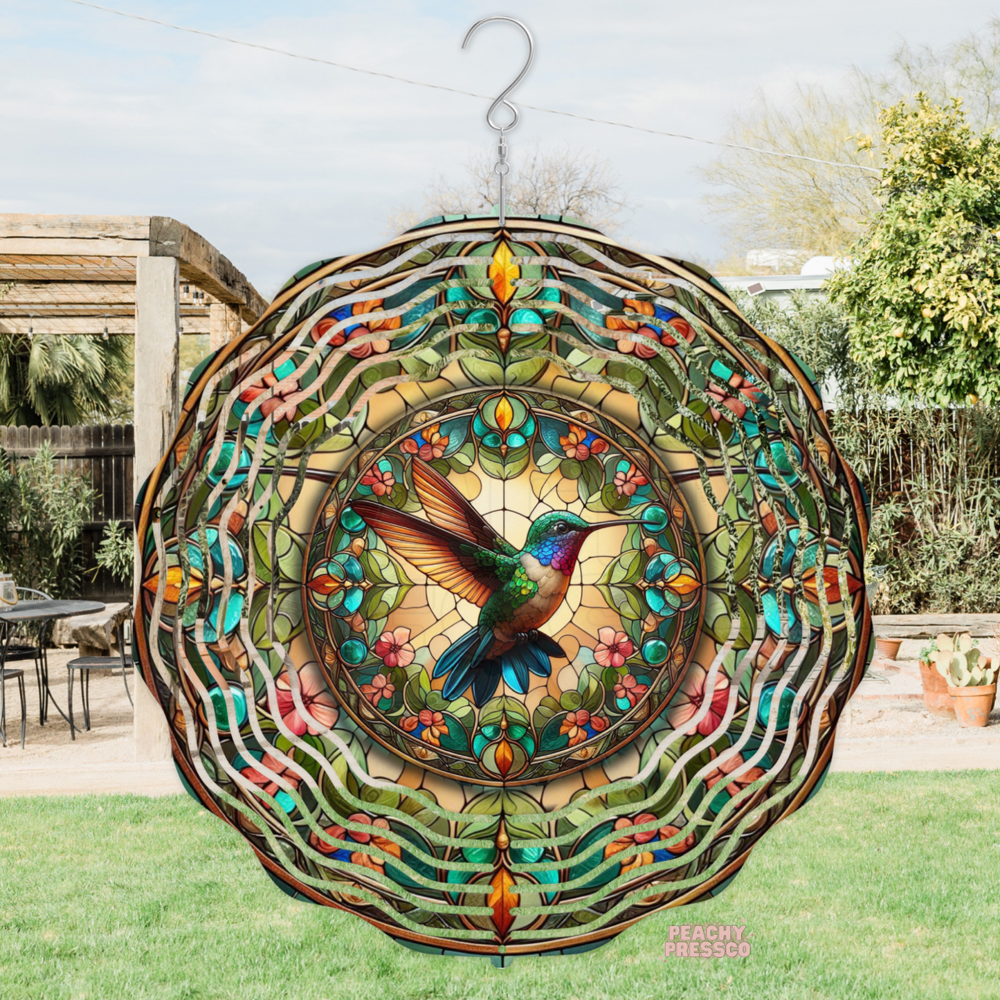 Decorative metal wind spinner with a stained glass style hummingbird surrounded by colorful flowers and leaves, creating a vibrant garden accent.