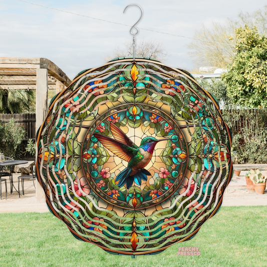 Decorative metal wind spinner with a stained glass style hummingbird surrounded by colorful flowers and leaves, creating a vibrant garden accent.