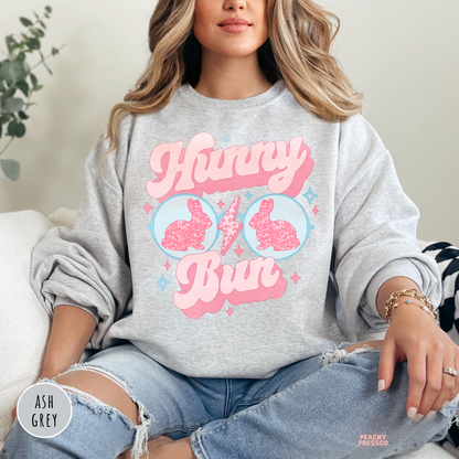 Woman wearing an ash grey sweatshirt with a retro Hunny Bun Easter bunny sunglasses graphic in pink and blue pastel colors.