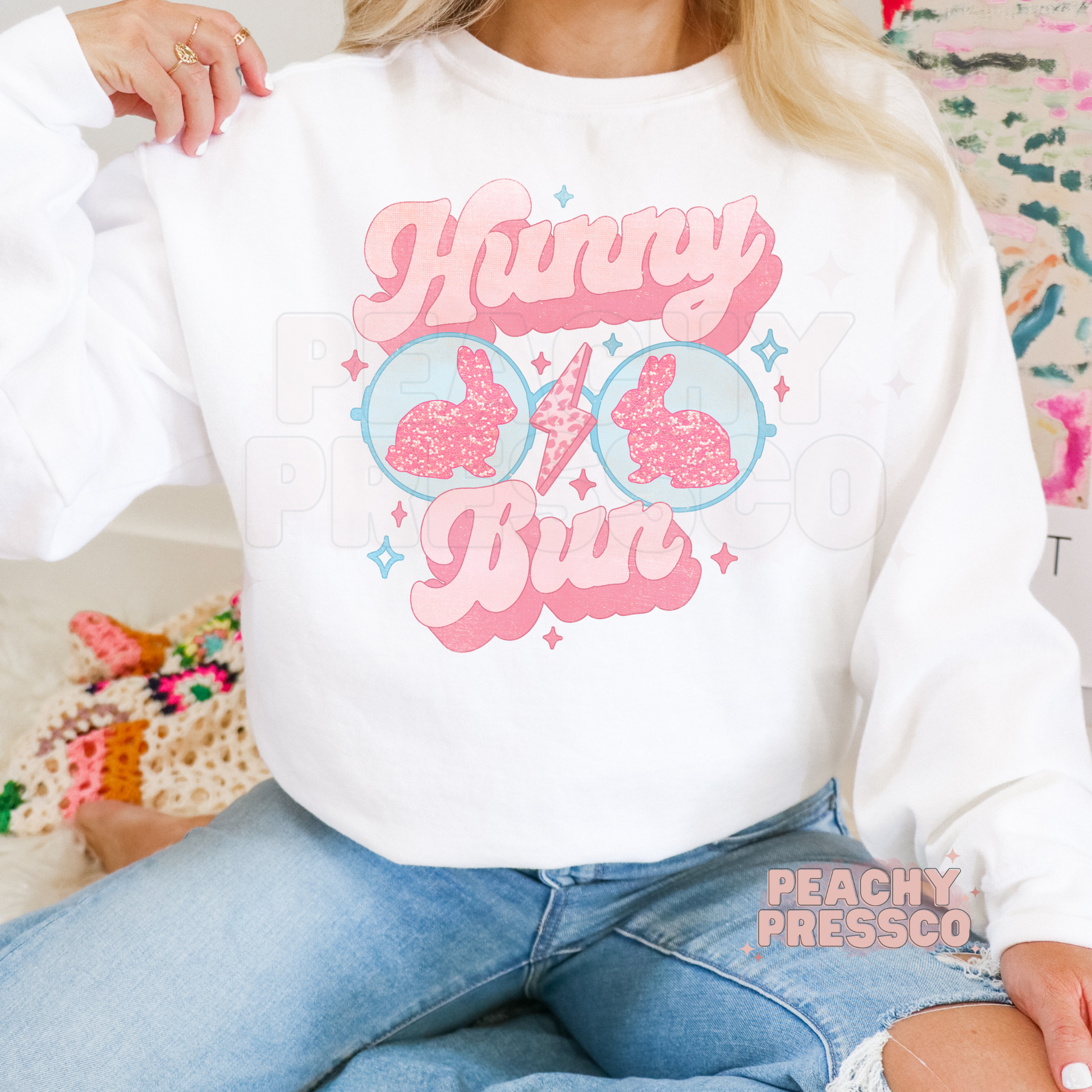 Woman wearing a white crewneck sweatshirt featuring a pastel Hunny Bun Easter bunny sunglasses graphic with retro spring aesthetic.