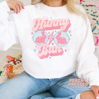 Woman wearing a white crewneck sweatshirt featuring a pastel Hunny Bun Easter bunny sunglasses graphic with retro spring aesthetic.