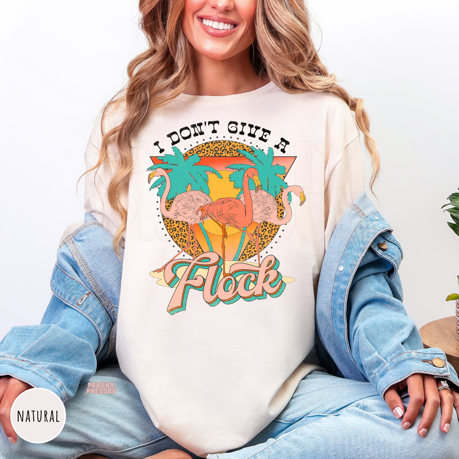 Natural Gildan unisex t-shirt featuring three pink flamingos, palm trees, and a retro sunset with the phrase "I Don't Give a Flock." Vintage tropical graphic tee perfect for summer, beach trips, vacations, pool parties, and flamingo fans.