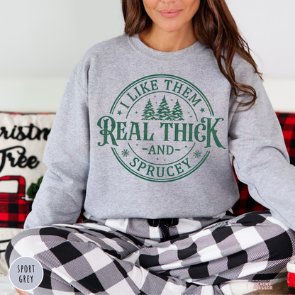 Women wearing a sport grey holiday sweatshirt printed with I Like Them Real Thick And Sprucey paired with black and white checkered pajama pants.