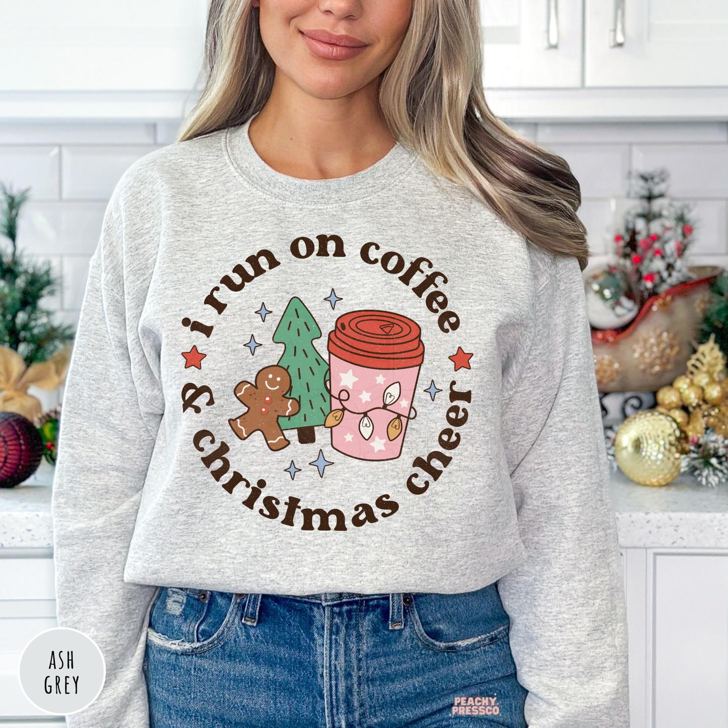Woman wearing an ash grey crewneck sweatshirt featuring "I Run On Coffee & Christmas Cheer" graphic with gingerbread man, tree, and holiday coffee cup.