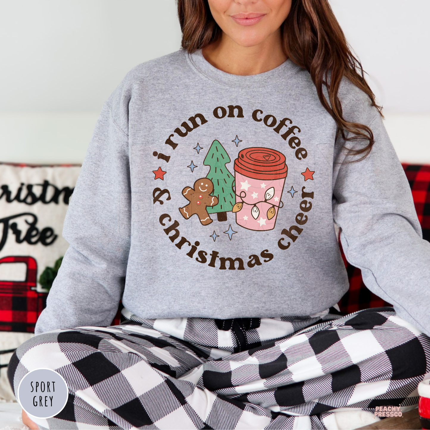 Women sitting in a sport grey coffee and Christmas cheer sweatshirt paired with black and white buffalo plaid pajama bottoms.