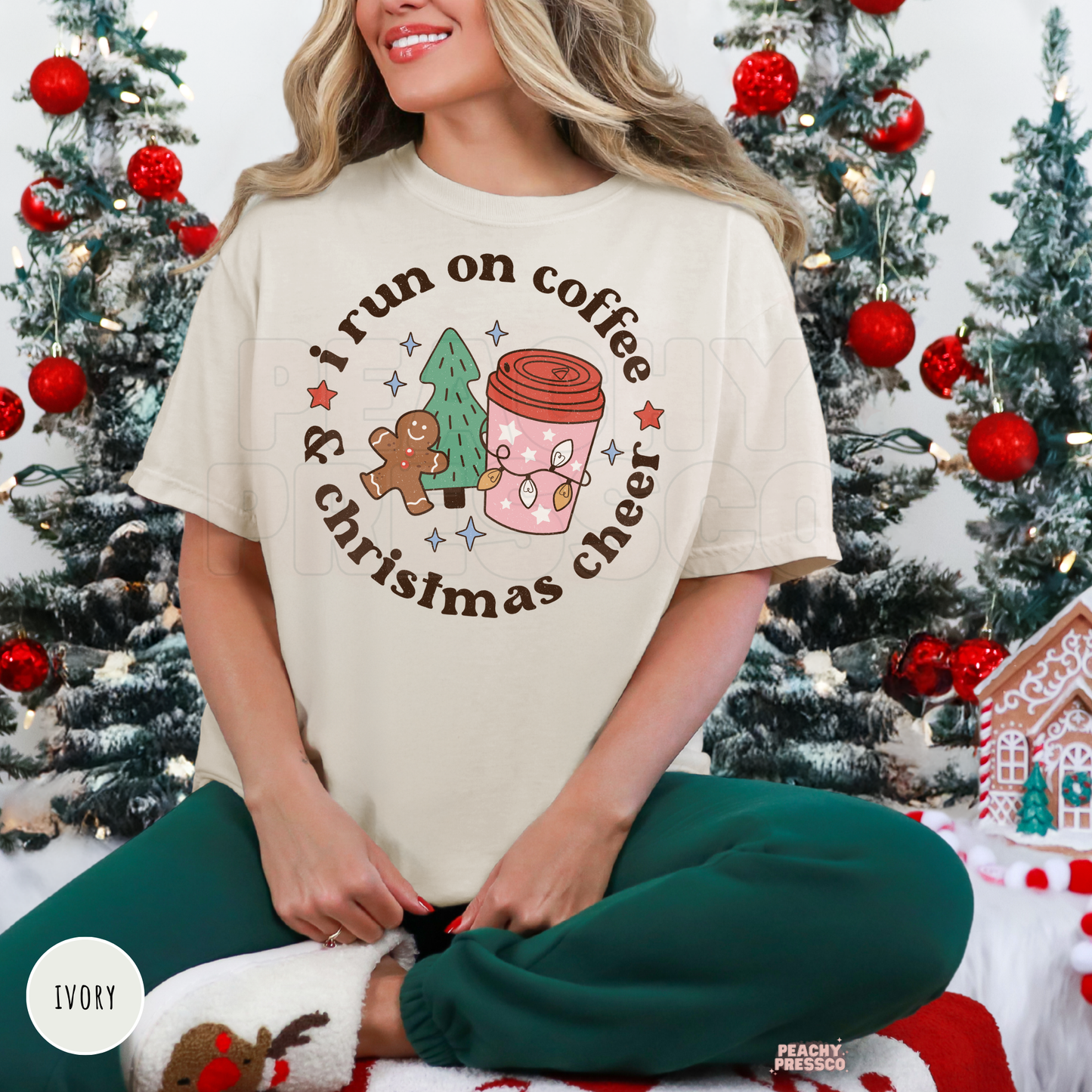 Woman sitting cross-legged wearing an ivory holiday coffee graphic t-shirt with green lounge pants.