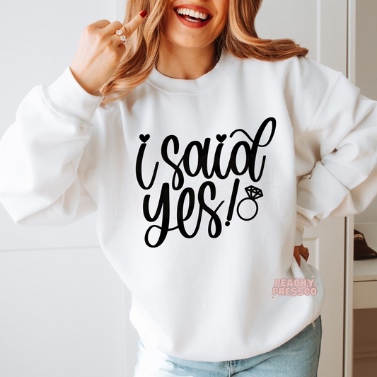 White crewneck sweatshirt featuring a modern "I Said Yes!" graphic with a sparkling engagement ring, perfect for engagement announcements, brides-to-be, bridal showers, bachelorette parties, and wedding gifts.