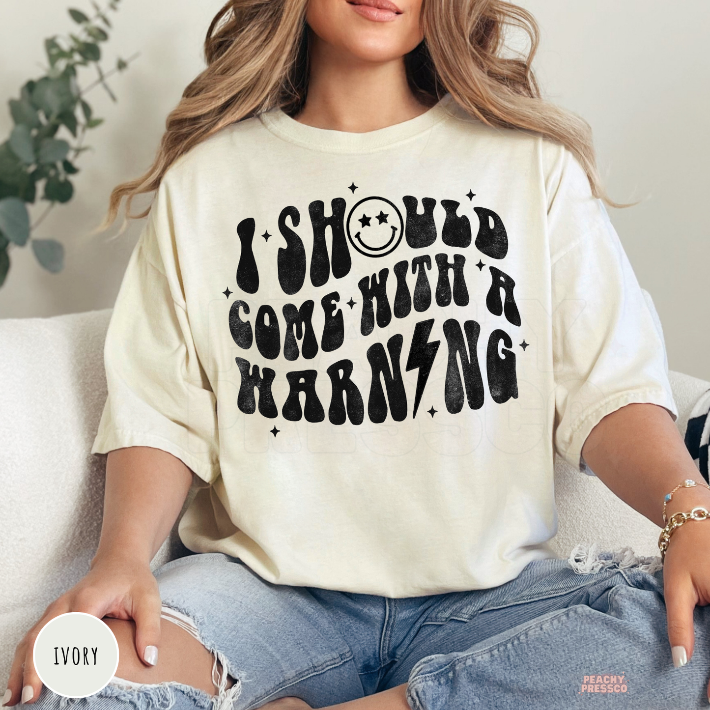 Woman wearing an ivory oversized t-shirt with the vintage "I Should Come With A Warning" graphic in black print.
