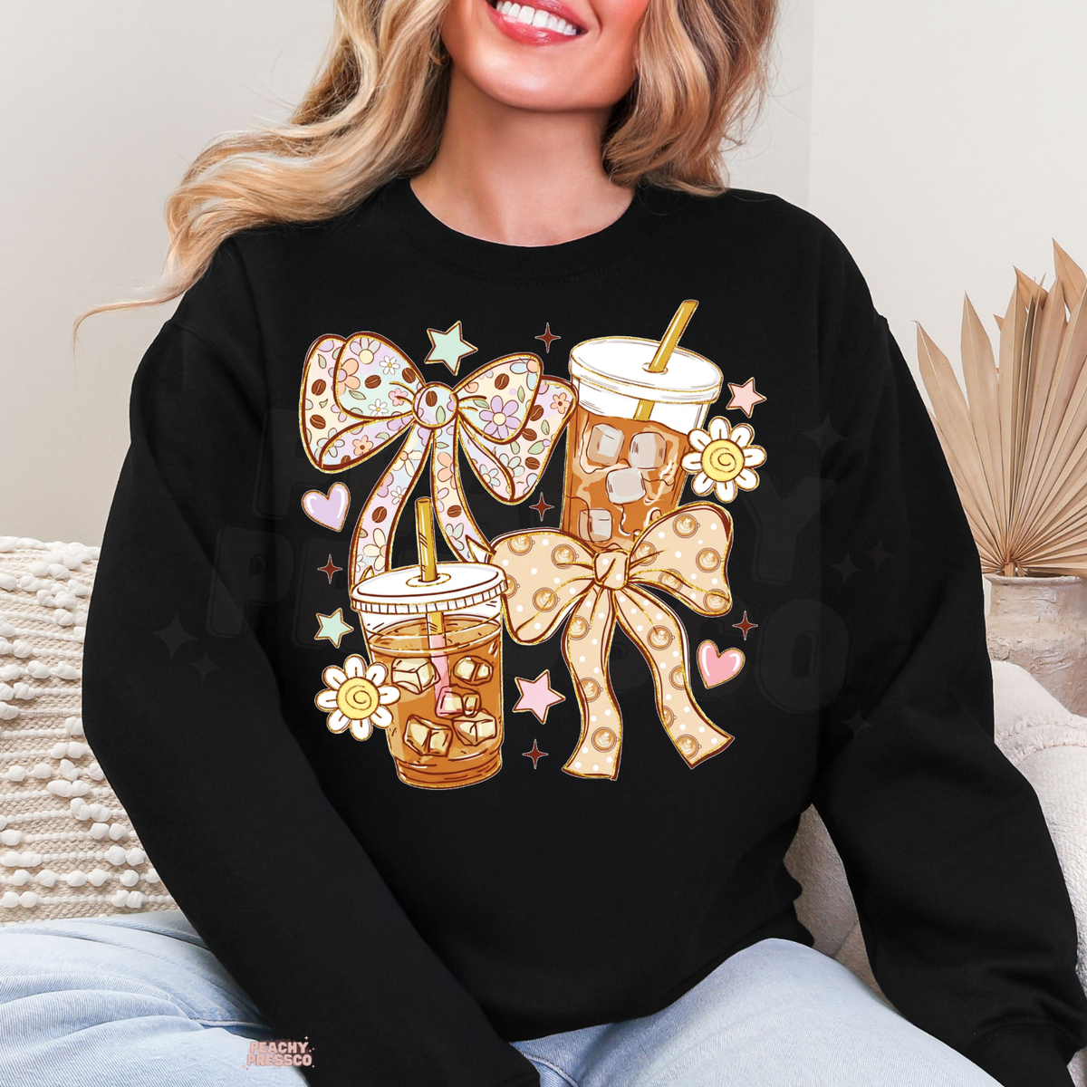 Black iced coffee sweatshirt with two caramel-coloured iced coffee illustrations, floral and polka dot coquette bows, pink hearts and cute daisies.