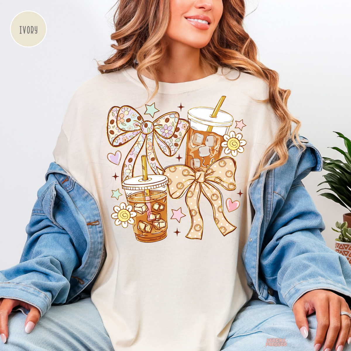 Ivory iced coffee shirt featuring two illustrated iced coffee cups, oversized floral and patterned bows, pastel hearts, daisies and stars.