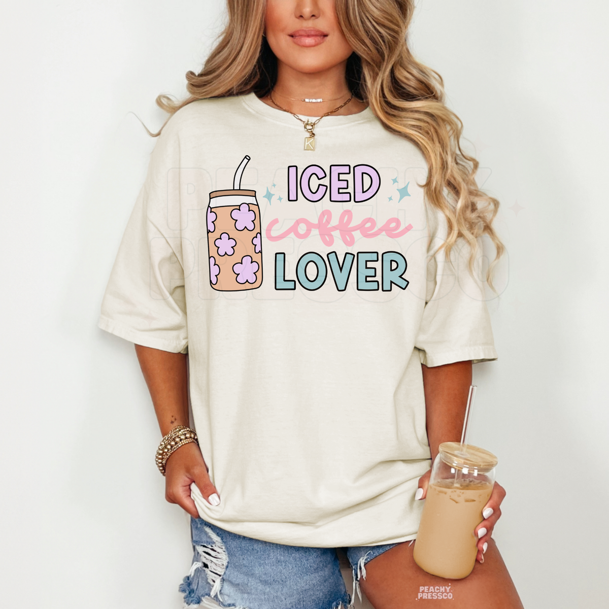 Ivory Iced Coffee Lover graphic t-shirt with pastel lettering, cute flower-patterned iced coffee tumbler and playful sparkles.
