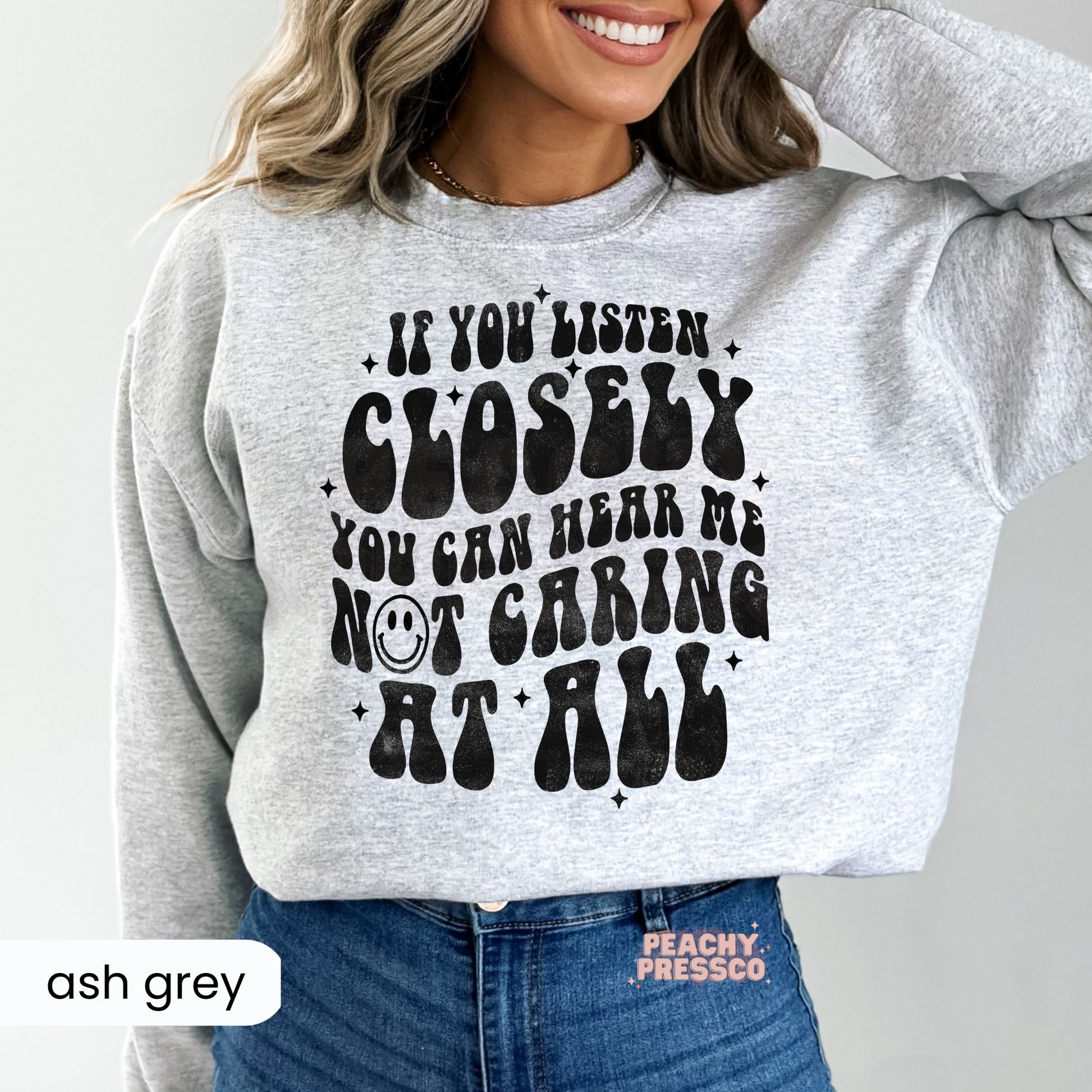 Ash grey crewneck sweatshirt with the sarcastic "If You Listen Closely You Can Hear Me Not Caring at All" graphic in distressed retro black text.