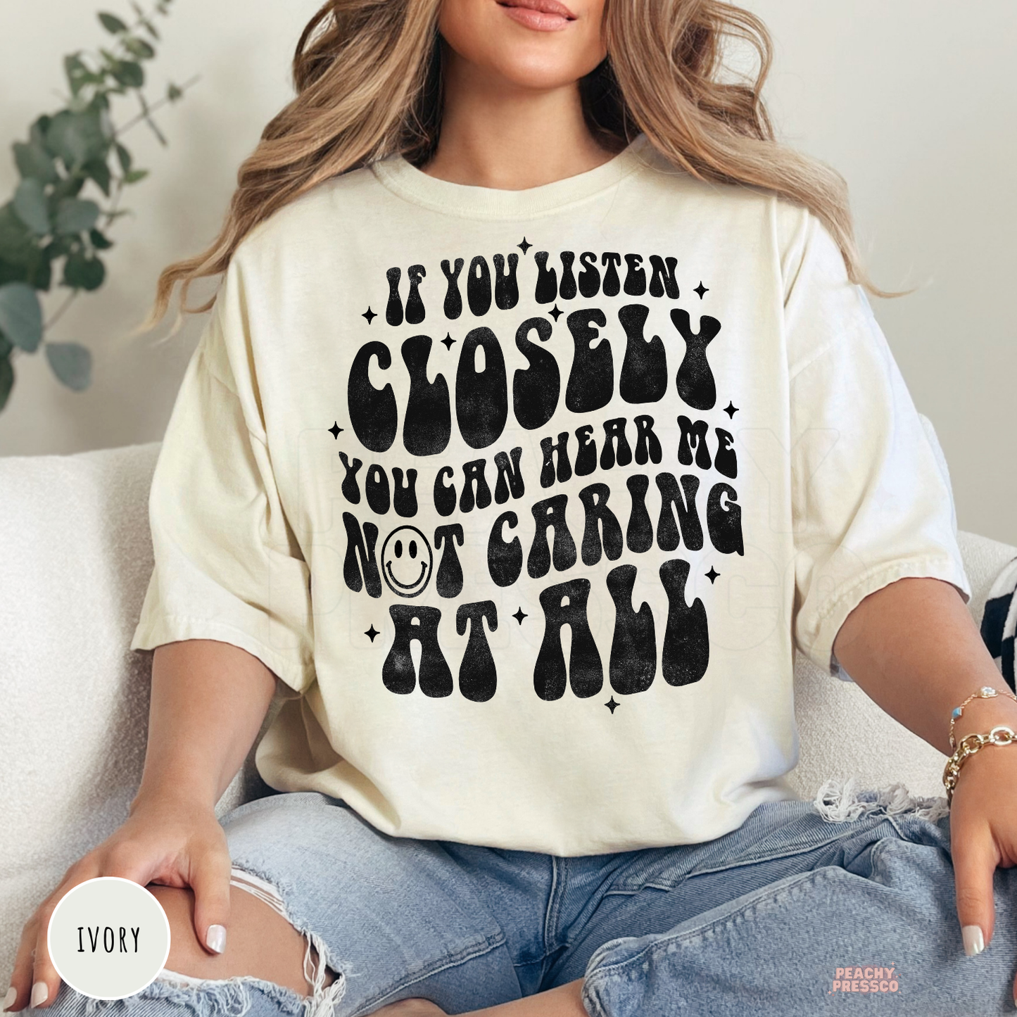 Ivory Comfort Colors graphic t-shirt featuring the sarcastic quote "If You Listen Closely You Can Hear Me Not Caring at All" in retro distressed black typography.