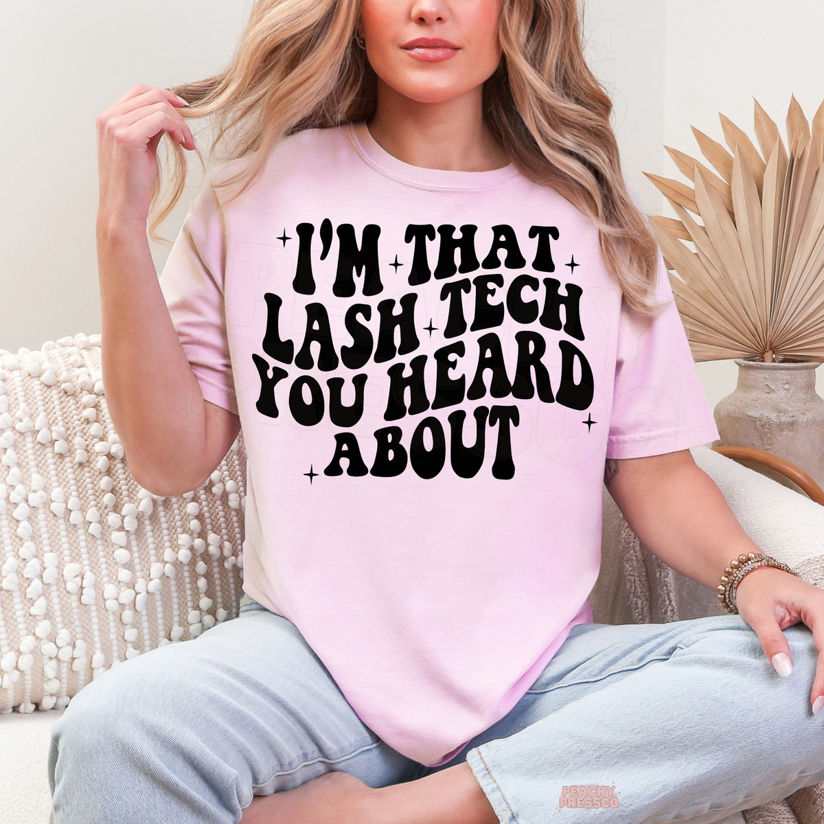 Woman wearing a light pink lash tech graphic T-shirt featuring the bold black I'm That Lash Tech You Heard About design with star accents.