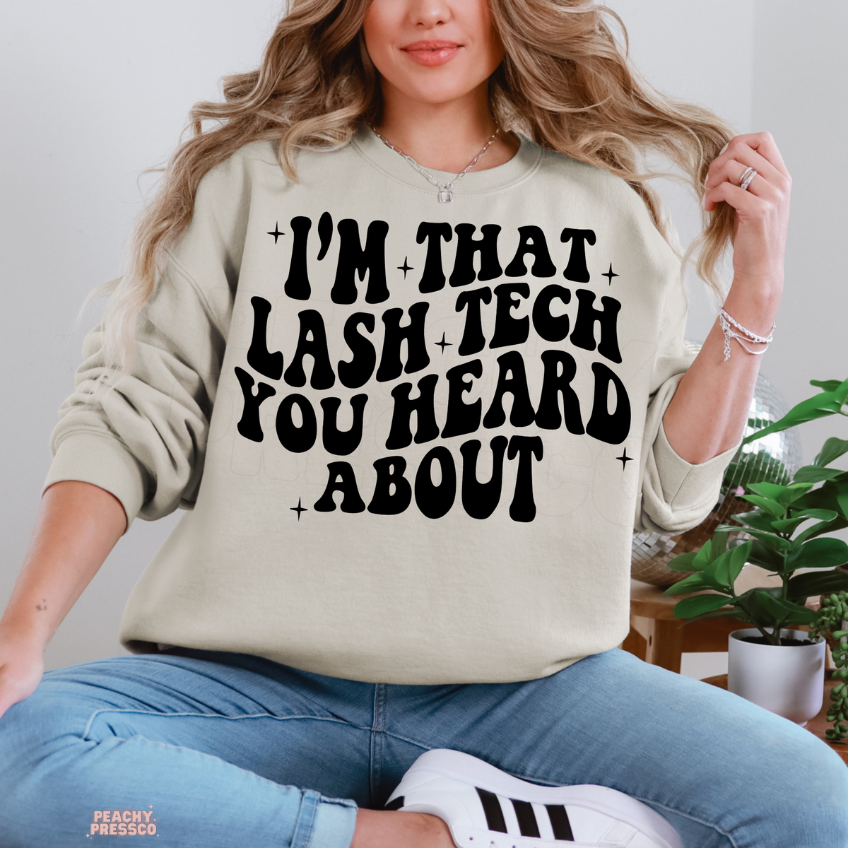 Woman wearing a sand coloured lash tech crewneck sweatshirt with the bold black I'm That Lash Tech You Heard About graphic.