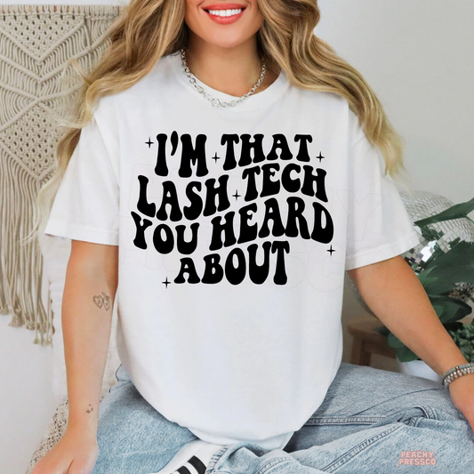 Woman wearing a white lash artist T-shirt with bold black I'm That Lash Tech You Heard About lettering and decorative stars.