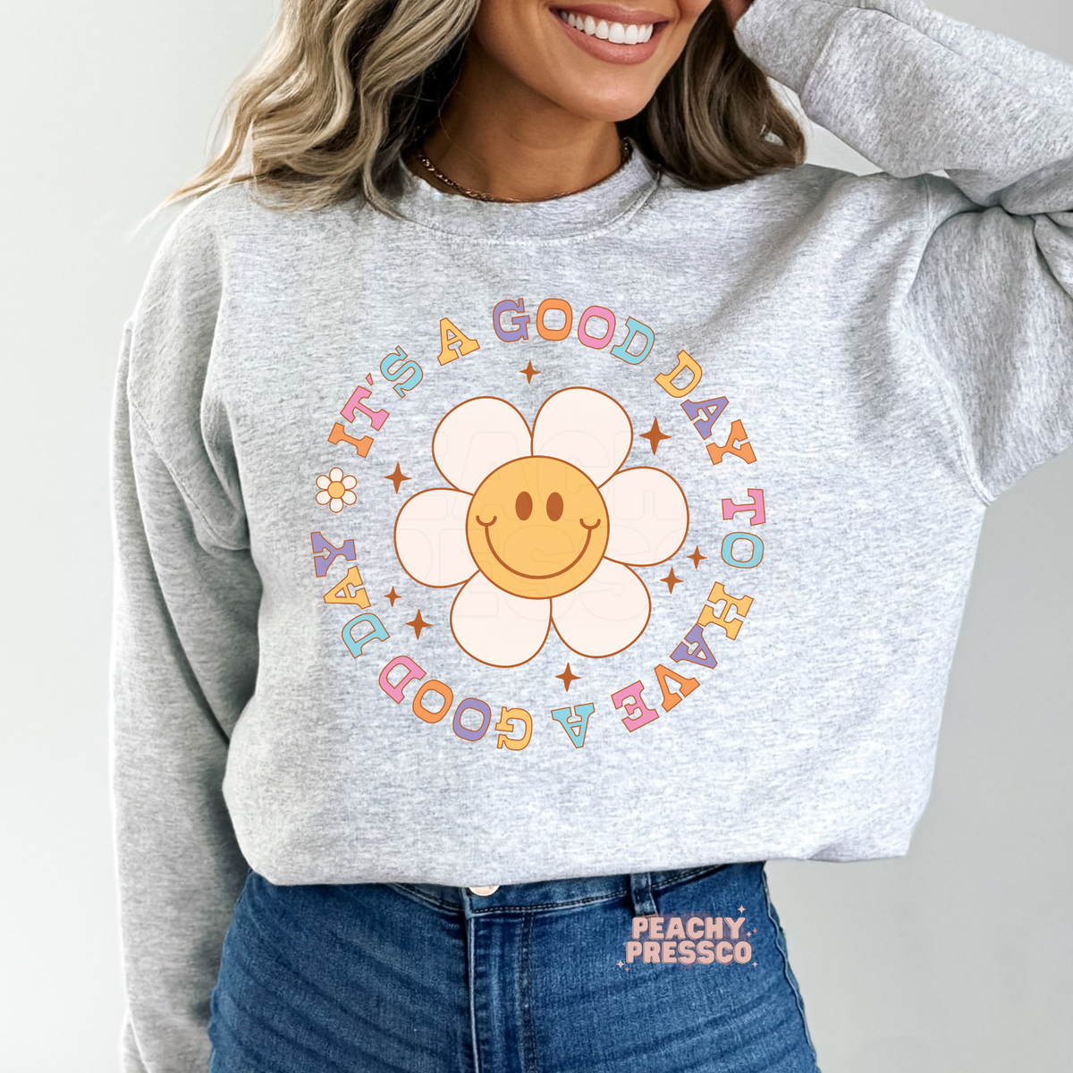 Ash grey sweatshirt with a retro smiley flower graphic and pastel typography featuring the uplifting quote "It's a Good Day to Have a Good Day."