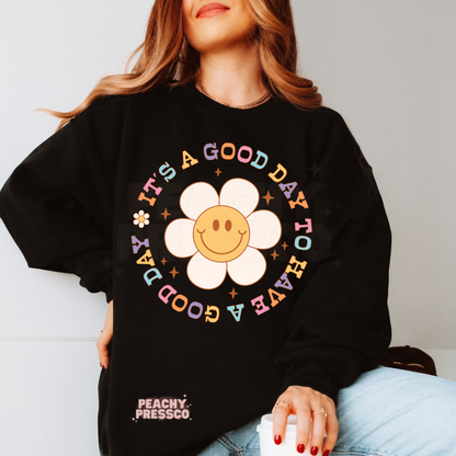 Black sweatshirt displaying a cheerful smiley daisy surrounded by pastel vintage lettering reading "It's a Good Day to Have a Good Day."