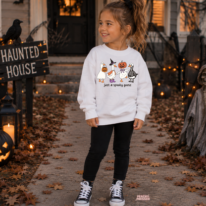 Girl wearing a white Just a Spooky Goose Halloween sweatshirt with cute costumed geese and pumpkin, witch and skeleton details.