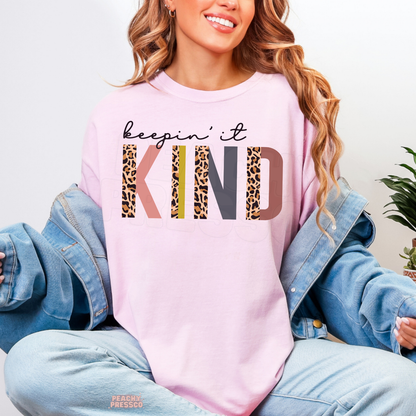 Light pink Keepin' It Kind shirt featuring retro multicolored KIND typography with leopard print details and an uplifting kindness quote.