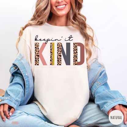 Natural Keepin' It Kind shirt featuring bold retro KIND lettering with leopard print, pink, mustard yellow, charcoal grey and brown accents.