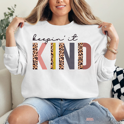 White Keepin' It Kind sweatshirt featuring oversized leopard print KIND lettering, playful retro colors and an inspirational message about kindness.