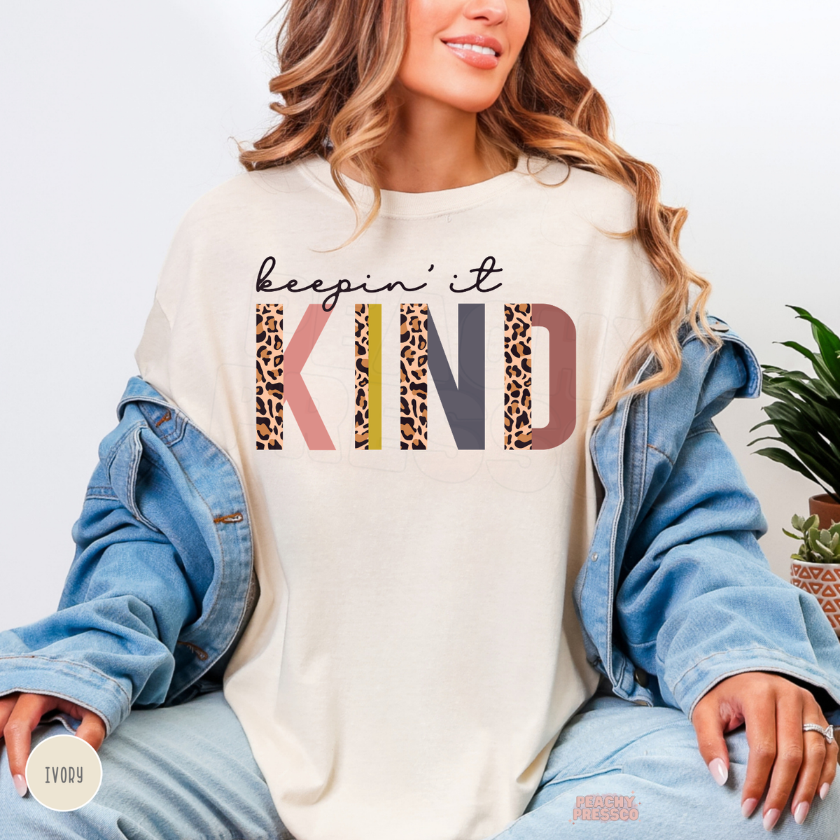 Ivory Keepin' It Kind sweatshirt with playful leopard print KIND lettering in pink, yellow, charcoal and brown, promoting positivity and kindness.