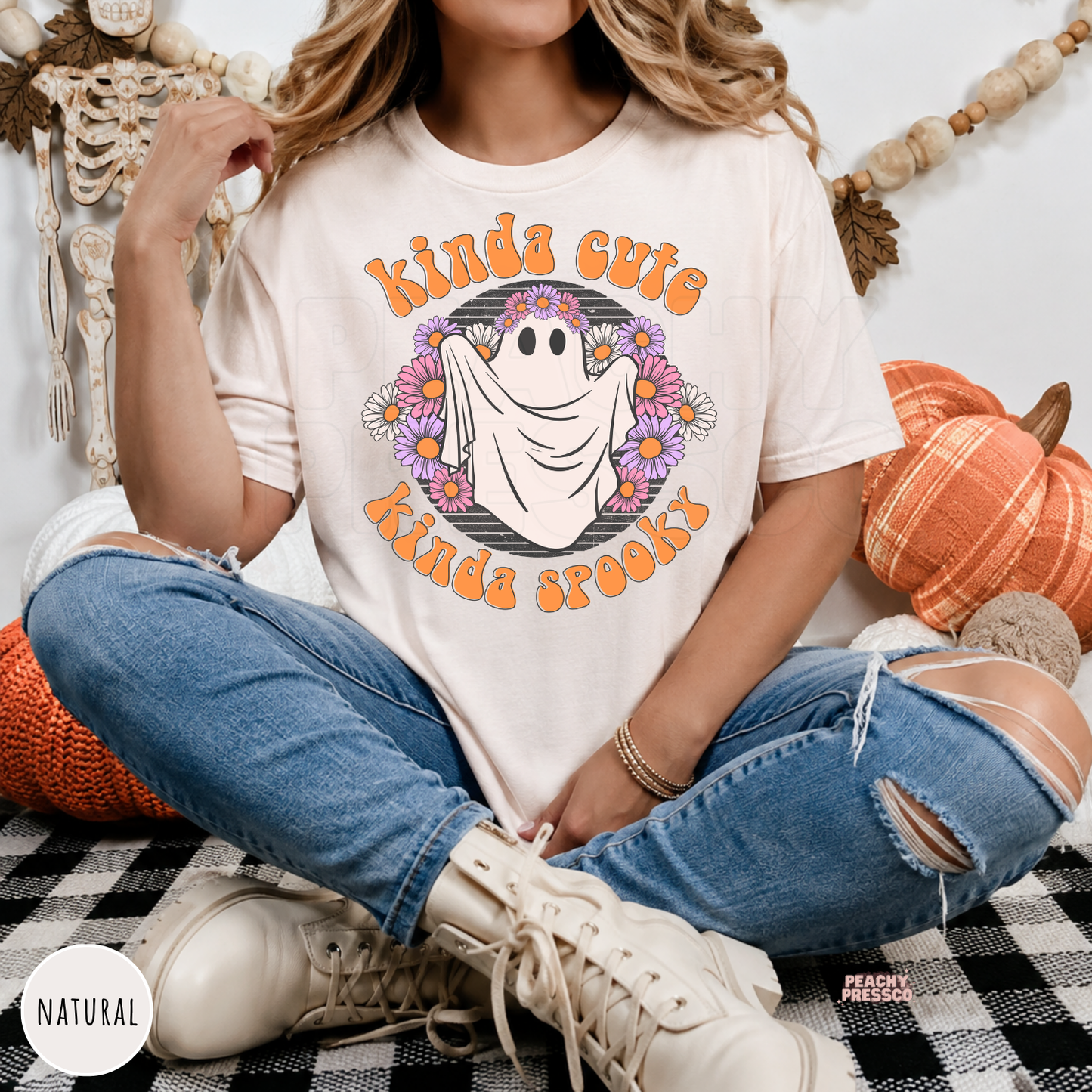 Woman wearing a natural Kinda Cute Kinda Spooky Halloween ghost graphic t-shirt featuring a smiling ghost surrounded by flowers.