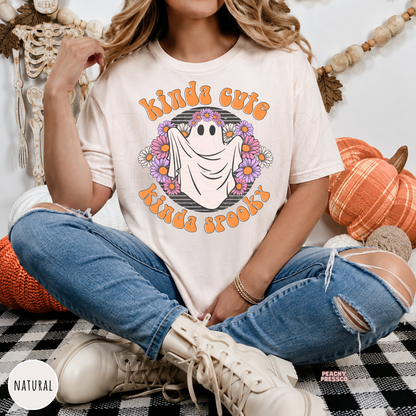 Woman wearing a natural Kinda Cute Kinda Spooky Halloween ghost graphic t-shirt featuring a smiling ghost surrounded by flowers.