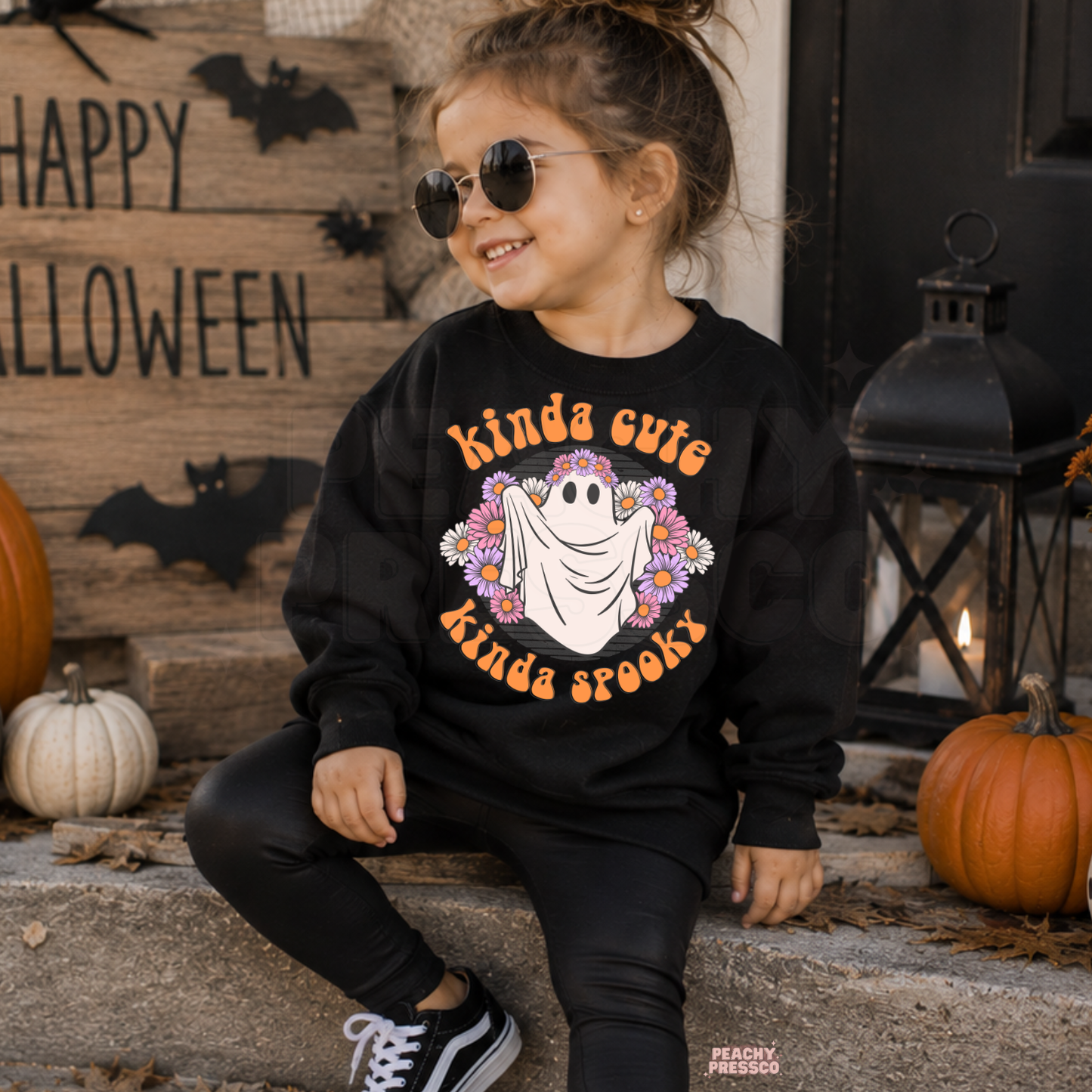 Girl wearing a black Kinda Cute Kinda Spooky Halloween sweatshirt featuring a cute floral ghost design with pumpkins and bats.