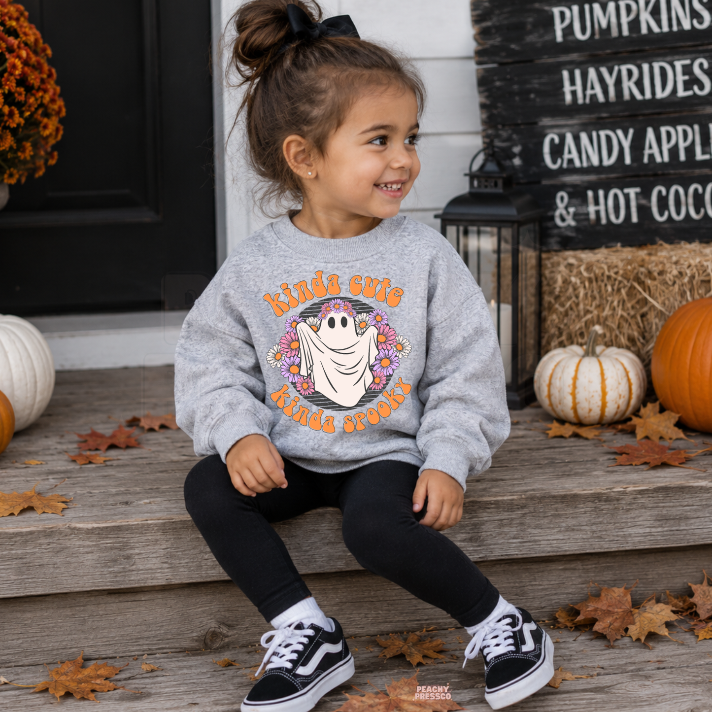 Girl wearing a sport grey Kinda Cute Kinda Spooky Halloween sweatshirt with a floral ghost graphic and fall pumpkin decor.