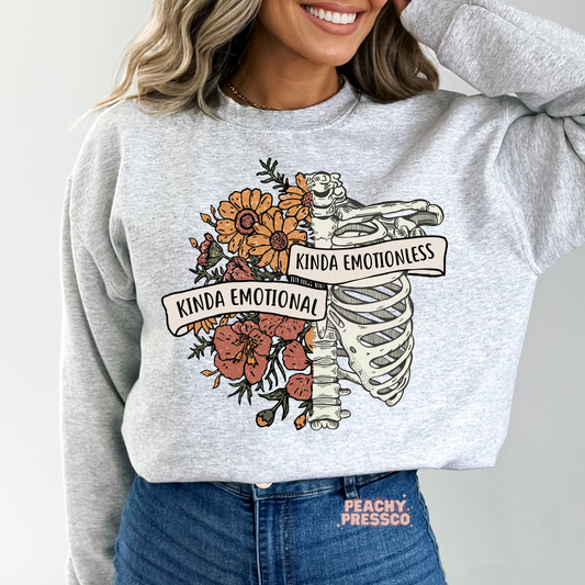 Ash grey sweatshirt featuring a split floral and skeleton ribcage illustration with "Kinda Emotional Kinda Emotionless" banner for a moody, vintage-inspired look.