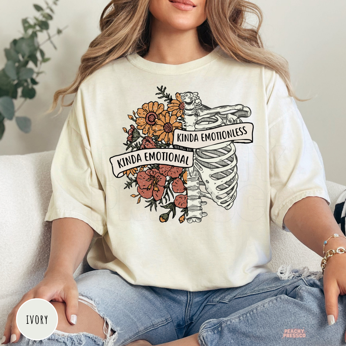Ivory Comfort Colors t-shirt featuring a floral ribcage illustration with the phrase "Kinda Emotional Kinda Emotionless," blending gothic art with vintage botanical style.