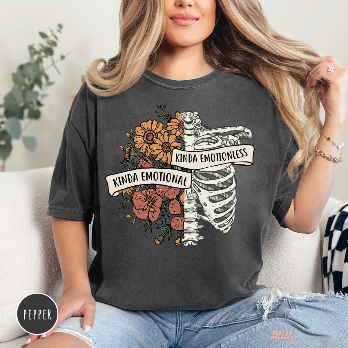 Pepper Comfort Colors t-shirt with a detailed skeleton and wildflower design featuring the quote "Kinda Emotional Kinda Emotionless" in a rustic vintage aesthetic.