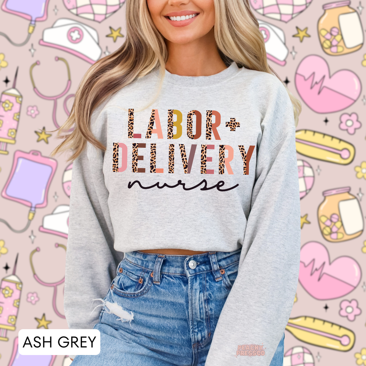 Ash grey Labor + Delivery nurse sweatshirt with playful leopard print lettering in pink and earthy tones, modeled with denim jeans against a nursing-themed background.