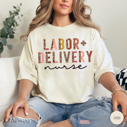 Ivory Labor + Delivery nurse T-shirt featuring leopard print and multicolored lettering with black cursive nurse text, styled with distressed blue jeans.