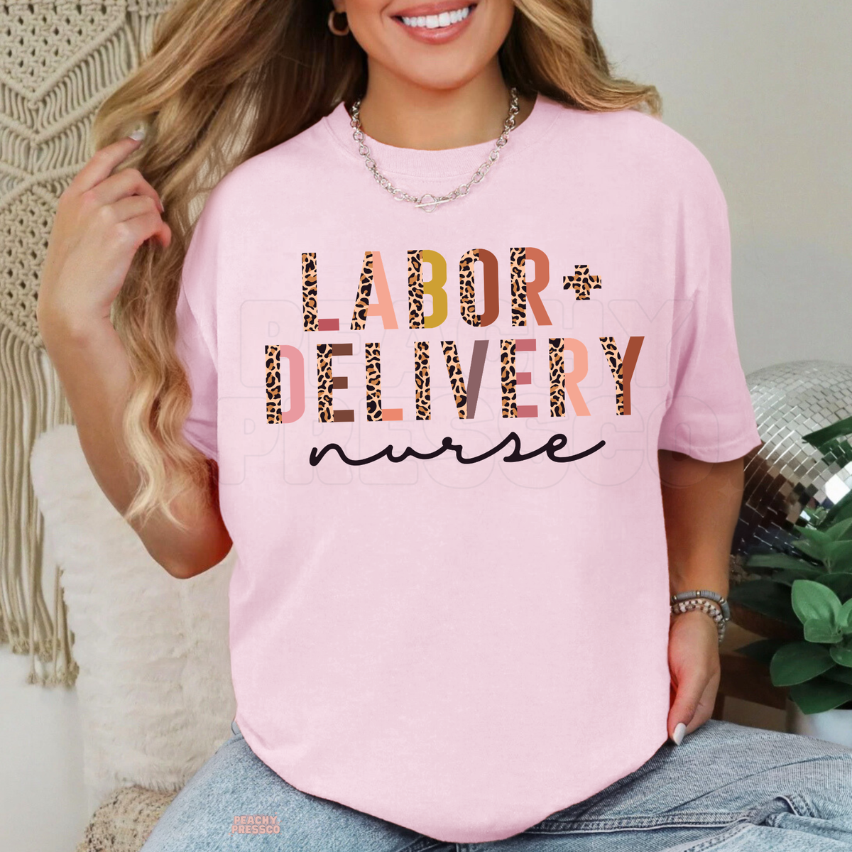 Light pink Labor and Delivery nurse T-shirt featuring bold leopard print and colorful lettering with black cursive nurse text, styled with blue jeans.