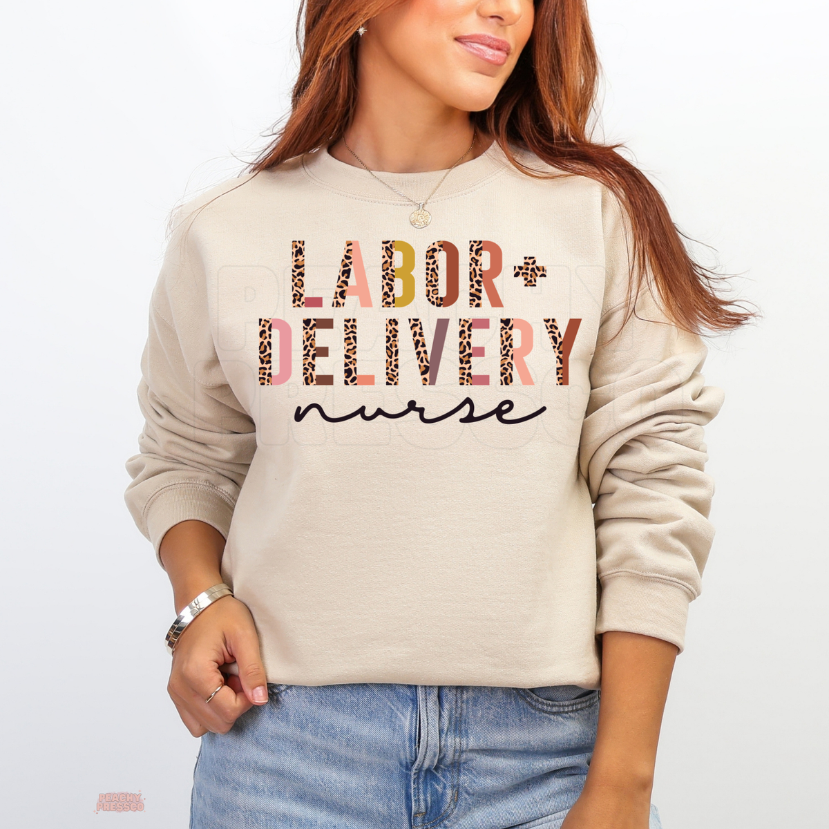 Sand-colored Labor and Delivery nurse sweatshirt featuring pink, peach and leopard print lettering with black cursive nurse text, styled with blue jeans.