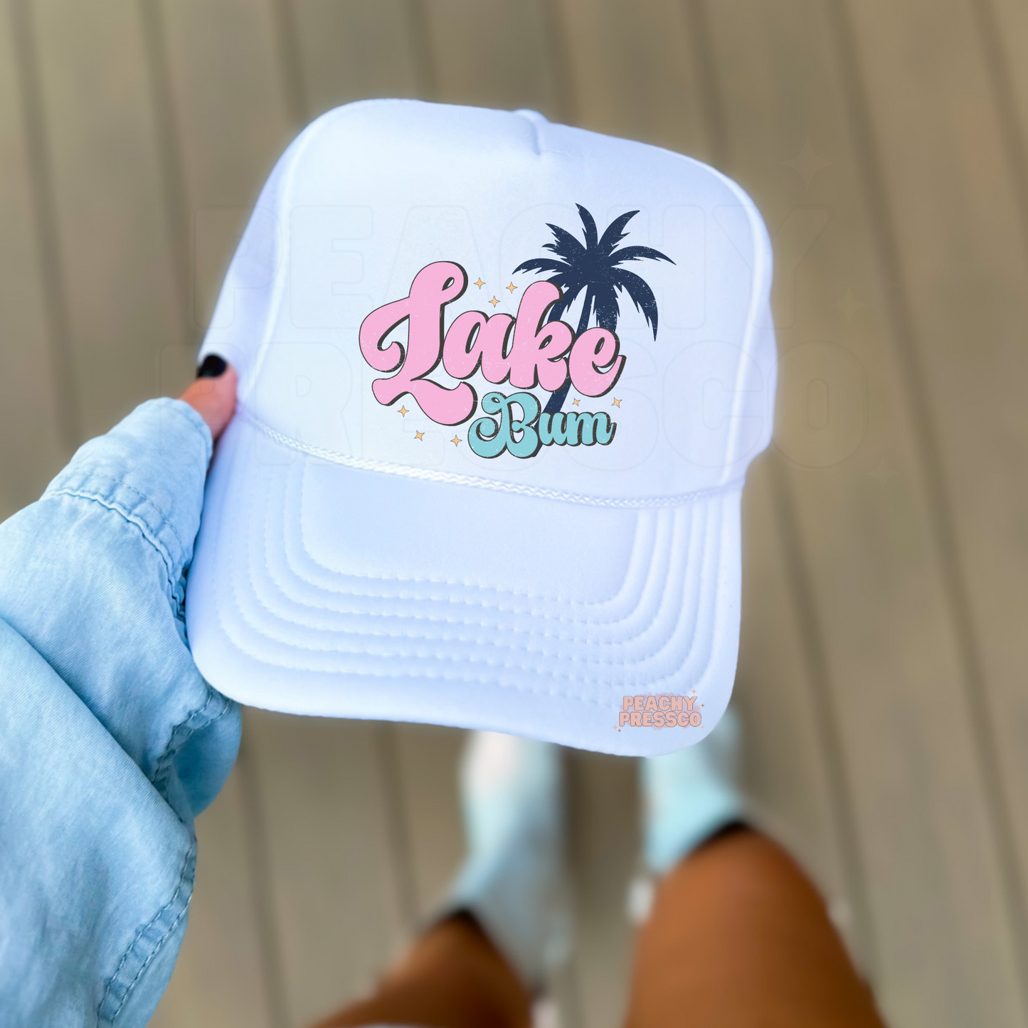 White foam trucker hat featuring a pastel "Lake Bum" design with a pink retro script, blue lettering, palm tree graphic, and subtle sparkles. Perfect for lake days, beach vacations, boating, camping, and summer adventures.
