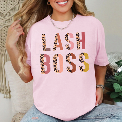 Woman wearing a light pink Lash Boss graphic T-shirt with bold leopard print lettering and colorful accents, perfect for lash artists.
