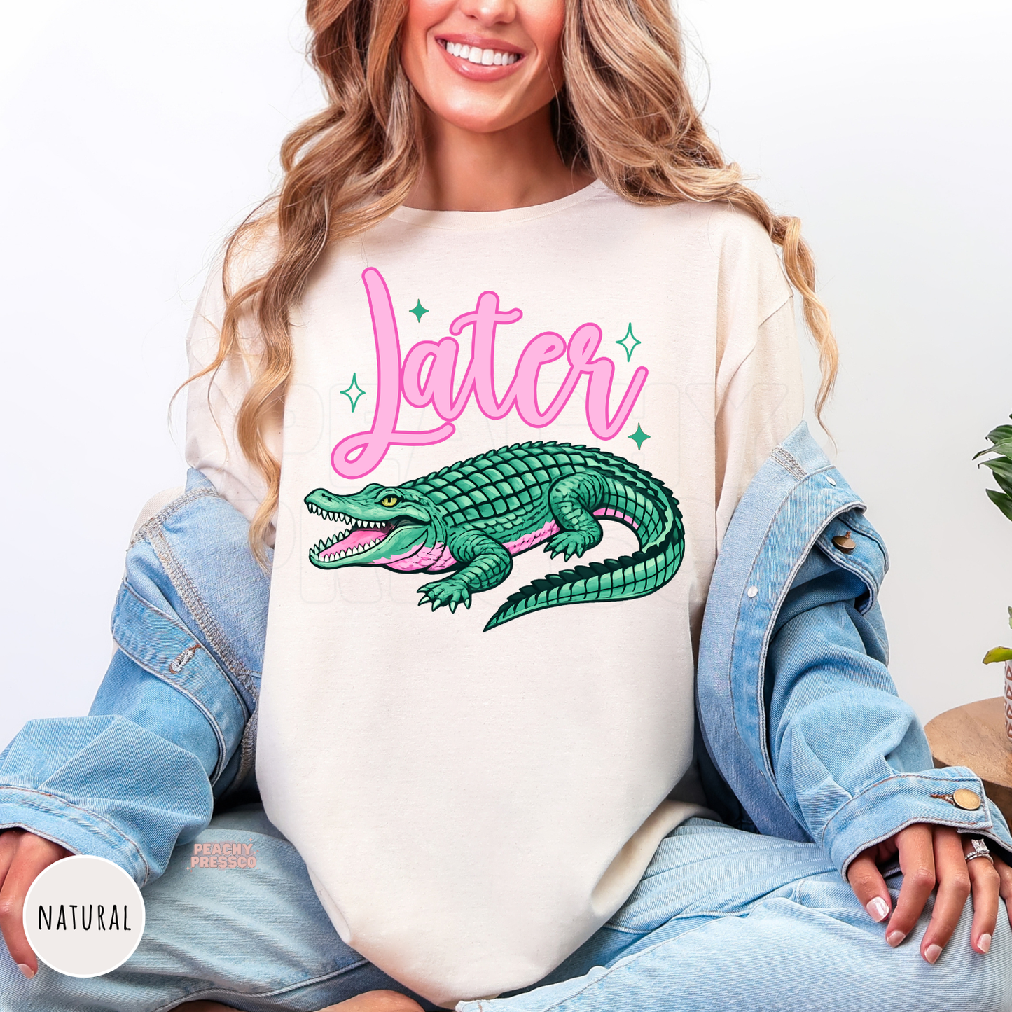 Woman wearing a natural unisex t-shirt featuring a retro pink "Later" script with a green alligator graphic. Playful Southern-inspired graphic tee with a vintage look, perfect for casual everyday outfits.