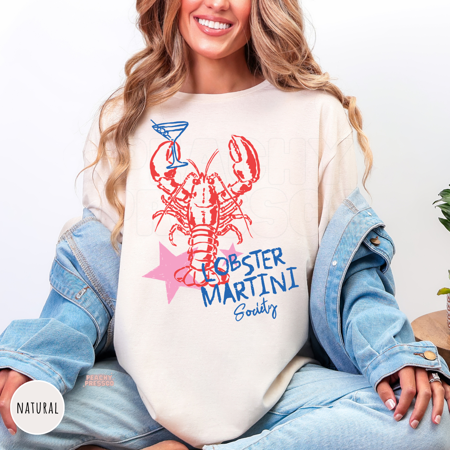 Natural Gildan unisex t-shirt featuring a bold red lobster, martini glass, pink star, and blue "Lobster Martini Society" design. Coastal graphic tee perfect for seafood lovers, beach vacations, summer gatherings, and New England-inspired style.