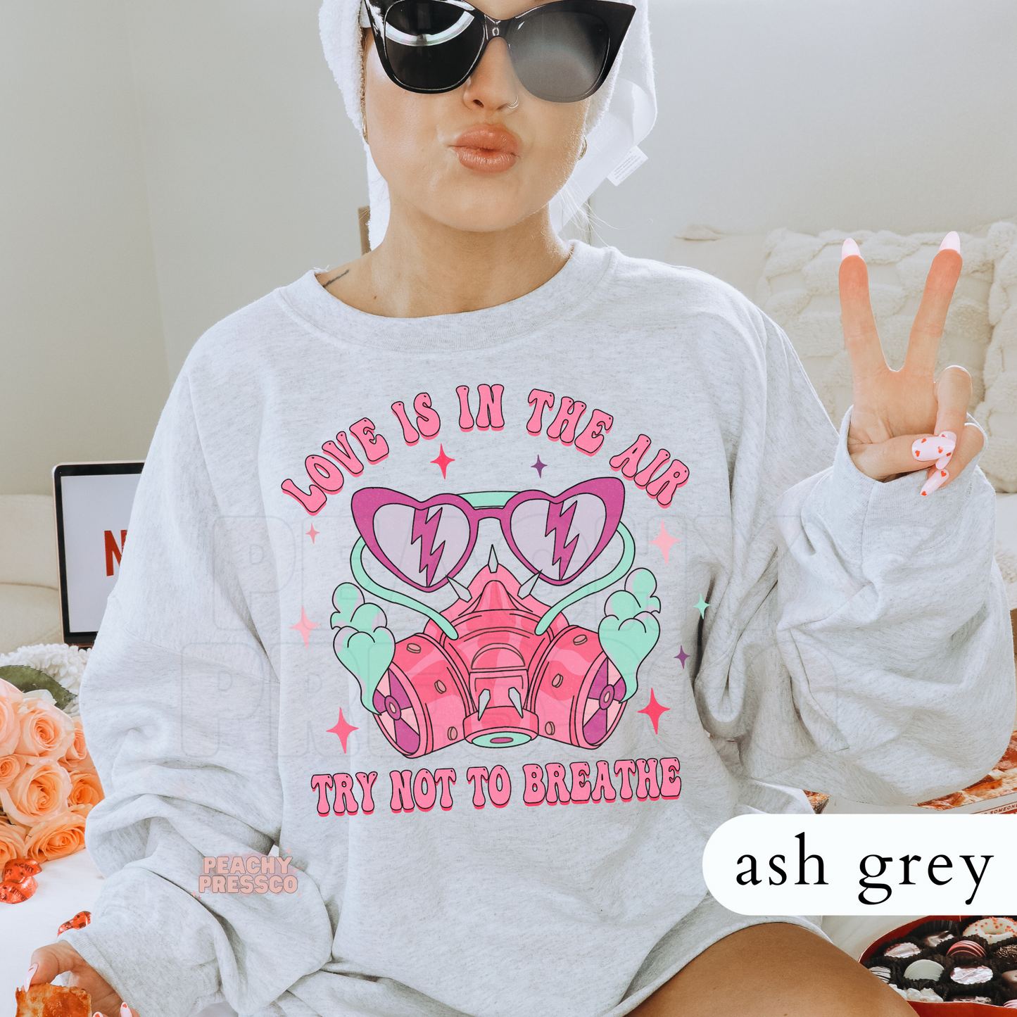 Love Is In The Air Try Not To Breathe design on an ash grey crewneck sweatshirt featuring a pink respirator mask, heart sunglasses, and retro Valentine's graphics.