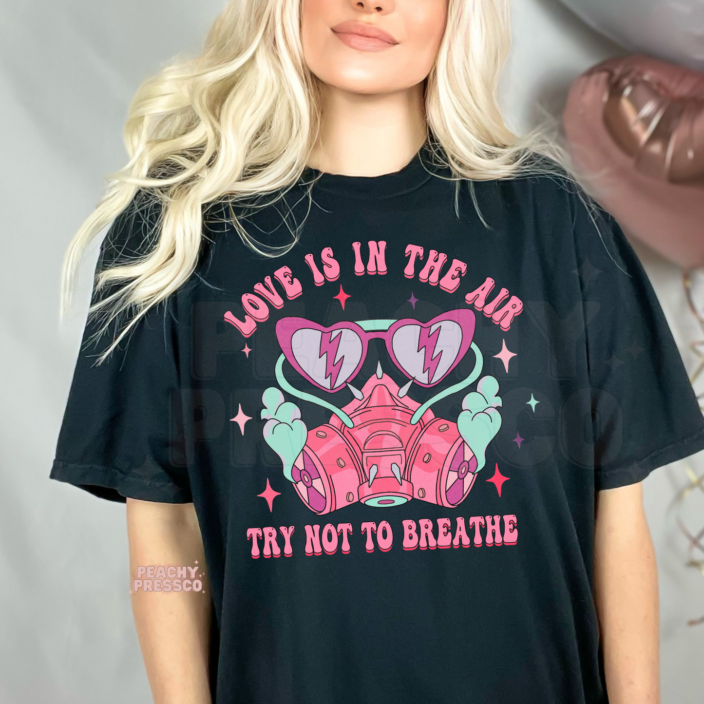 Funny Love Is In The Air Try Not To Breathe graphic on a black unisex t-shirt with retro pink respirator mask, pastel hearts, and Valentine's design.