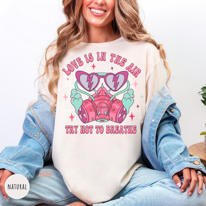 Love Is In The Air Try Not To Breathe graphic printed on a natural unisex shirt featuring a retro pink respirator mask, heart sunglasses, and Valentine's Day design.