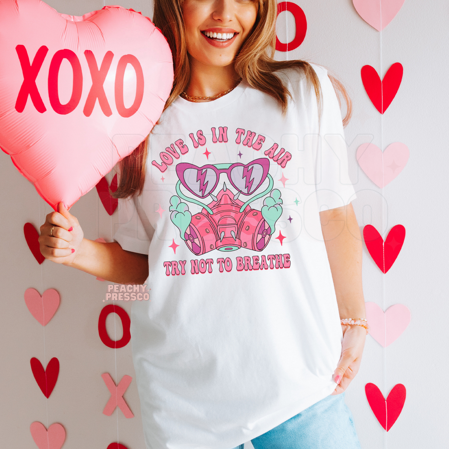 Love Is In The Air Try Not To Breathe retro Valentine's graphic printed on a white unisex t-shirt featuring a pink respirator mask and heart sunglasses.
