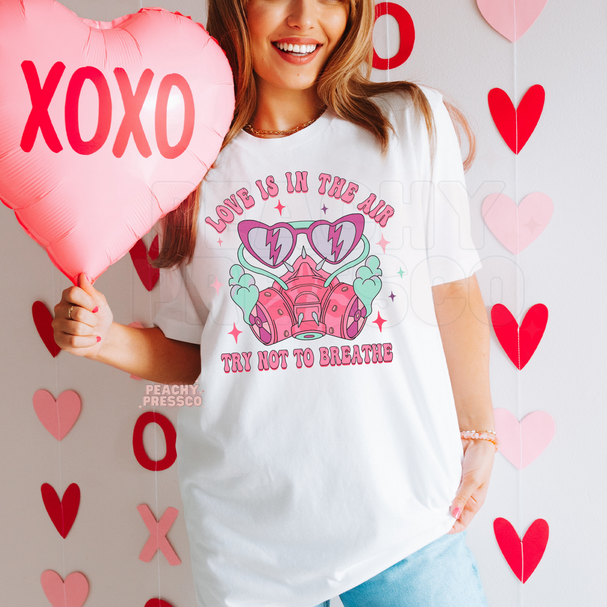 Love Is In The Air Try Not To Breathe retro Valentine's graphic printed on a white unisex t-shirt featuring a pink respirator mask and heart sunglasses.