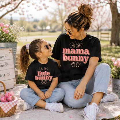 Mother and daughter wearing matching black Mama Bunny and Little Bunny Easter t-shirts while sitting together in a blooming spring garden with Easter décor.