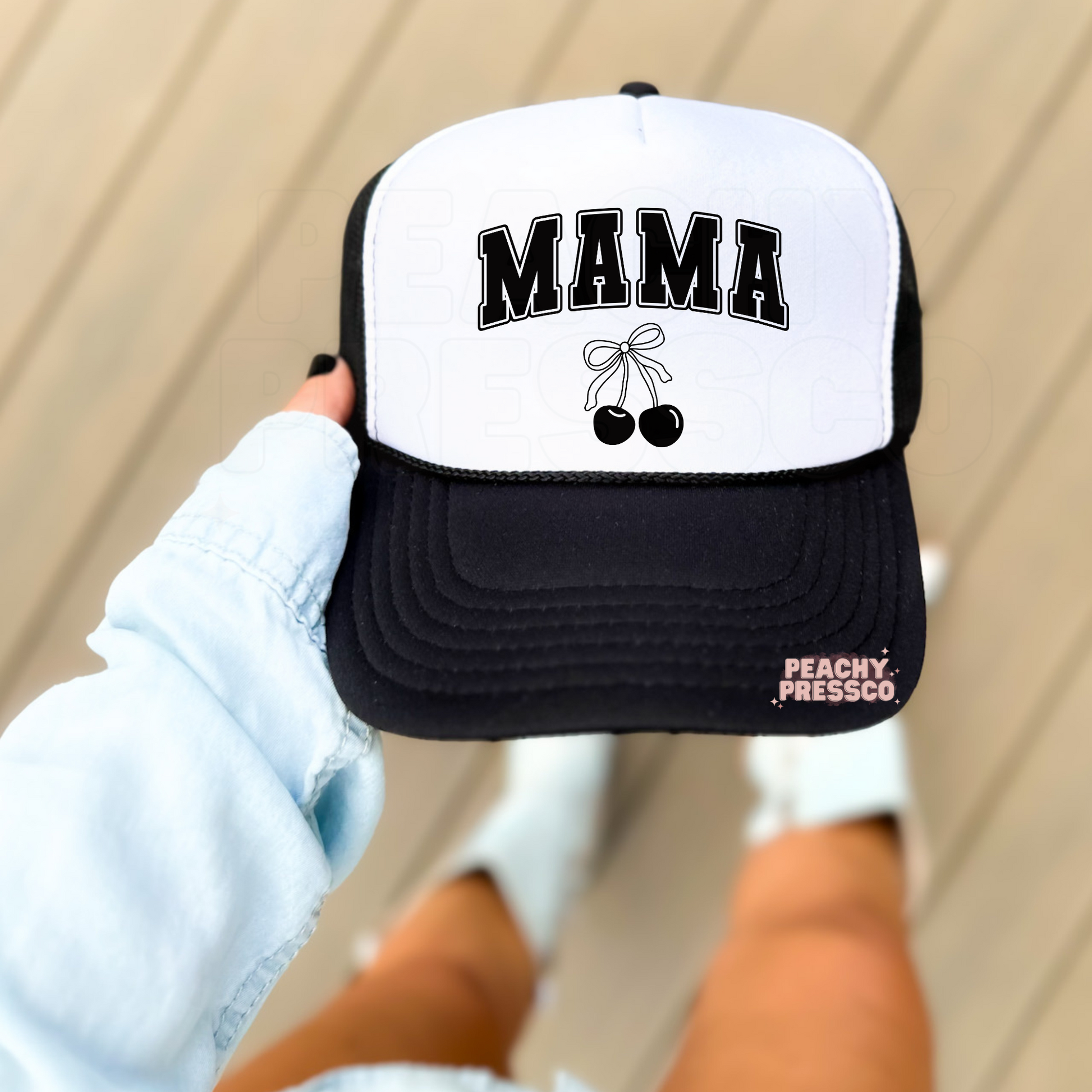 Black and white foam trucker hat featuring bold varsity "MAMA" lettering with a minimalist black cherry bow graphic. Trendy mama trucker hat perfect for everyday wear, Mother's Day, errands, vacations, and casual outfits.