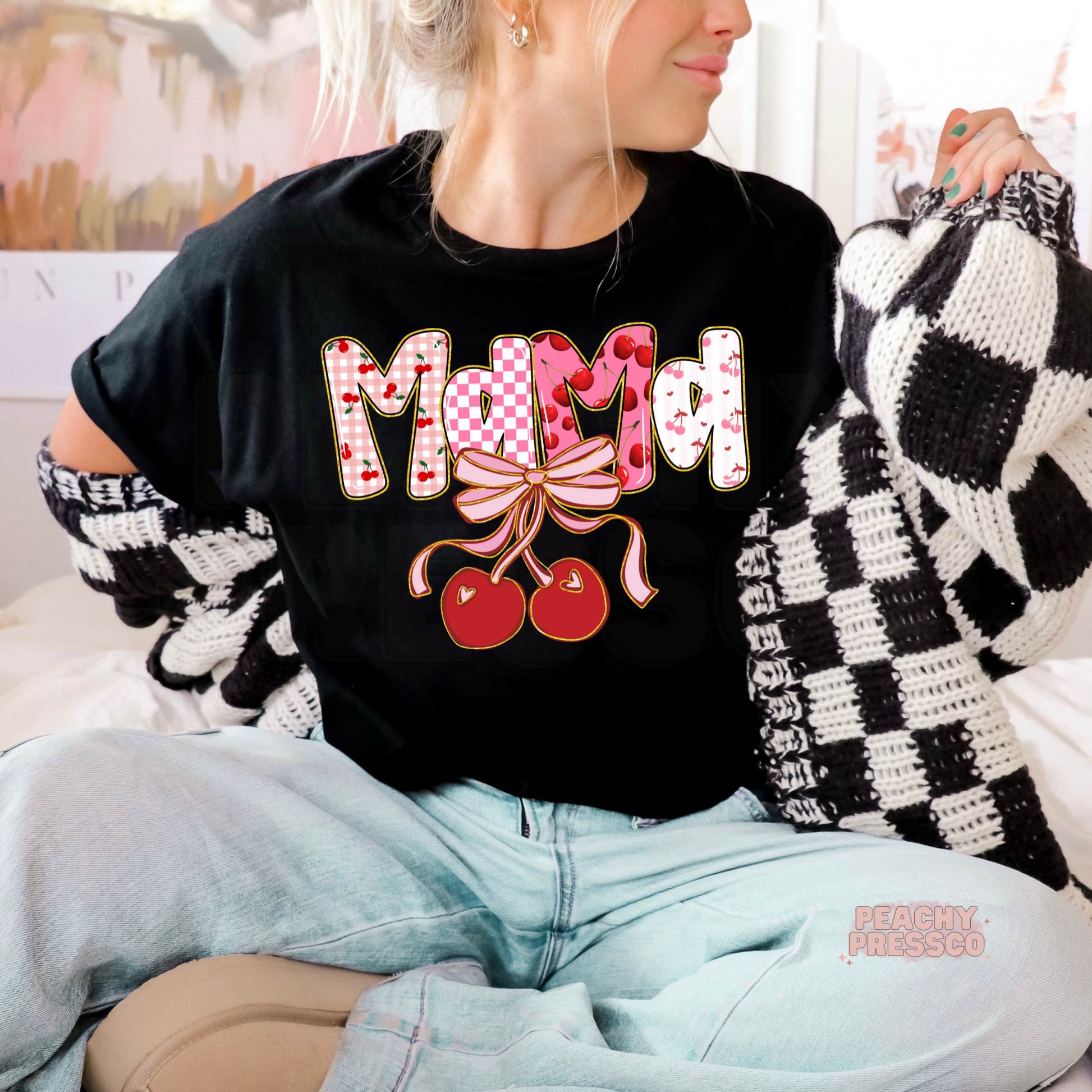 Woman wearing a black t-shirt with a cute Mama cherry bow design featuring pink cherry patterns and coquette-inspired artwork.